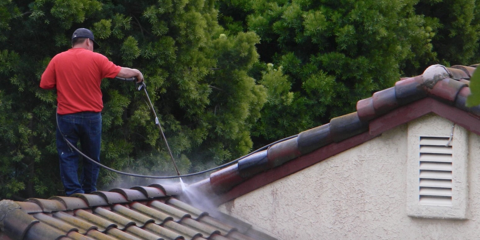 Man pressure washing a tile roof to clean it